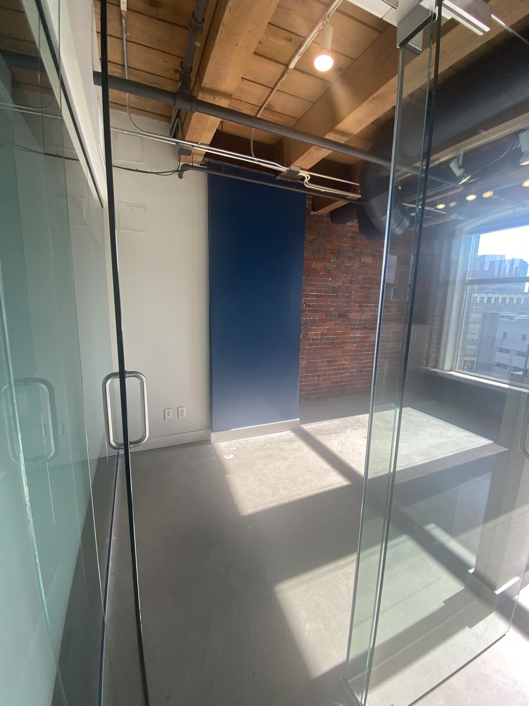 Glass-walled office with a navy feature wall, exposed brick and a heavy-timber ceiling