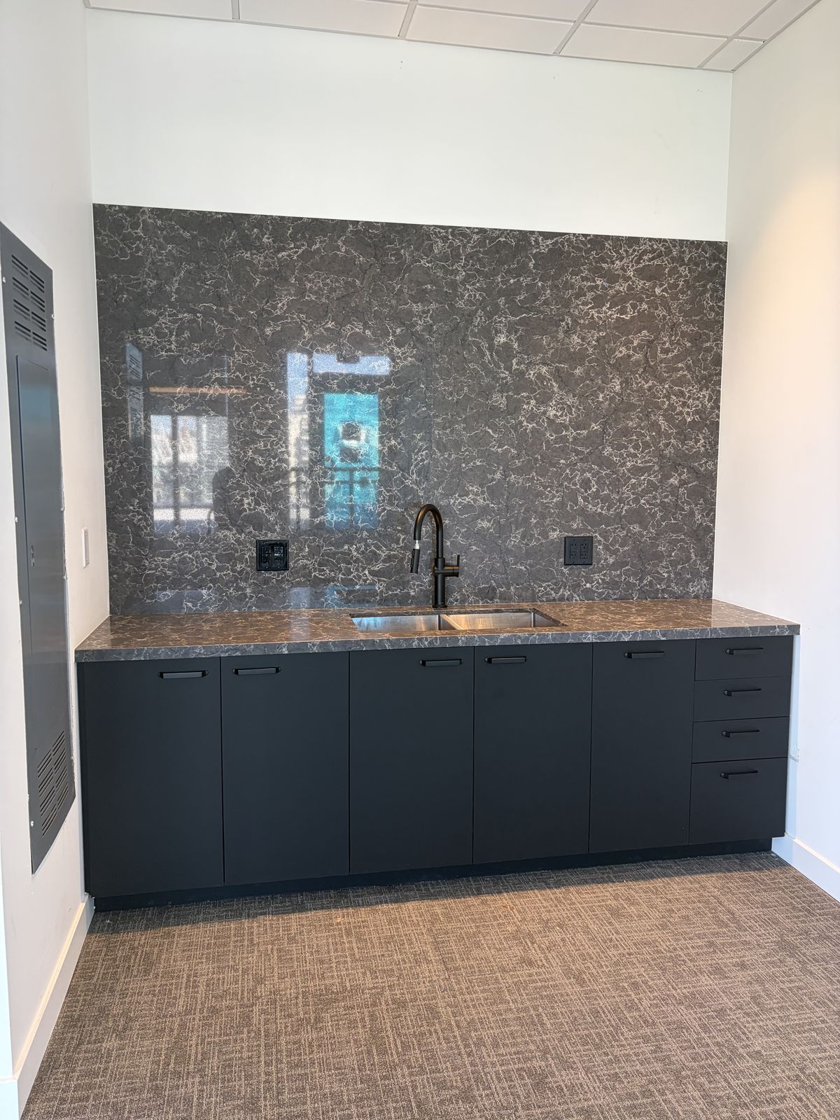 Kitchenette with dark cabinetry and a patterned stone backsplash
