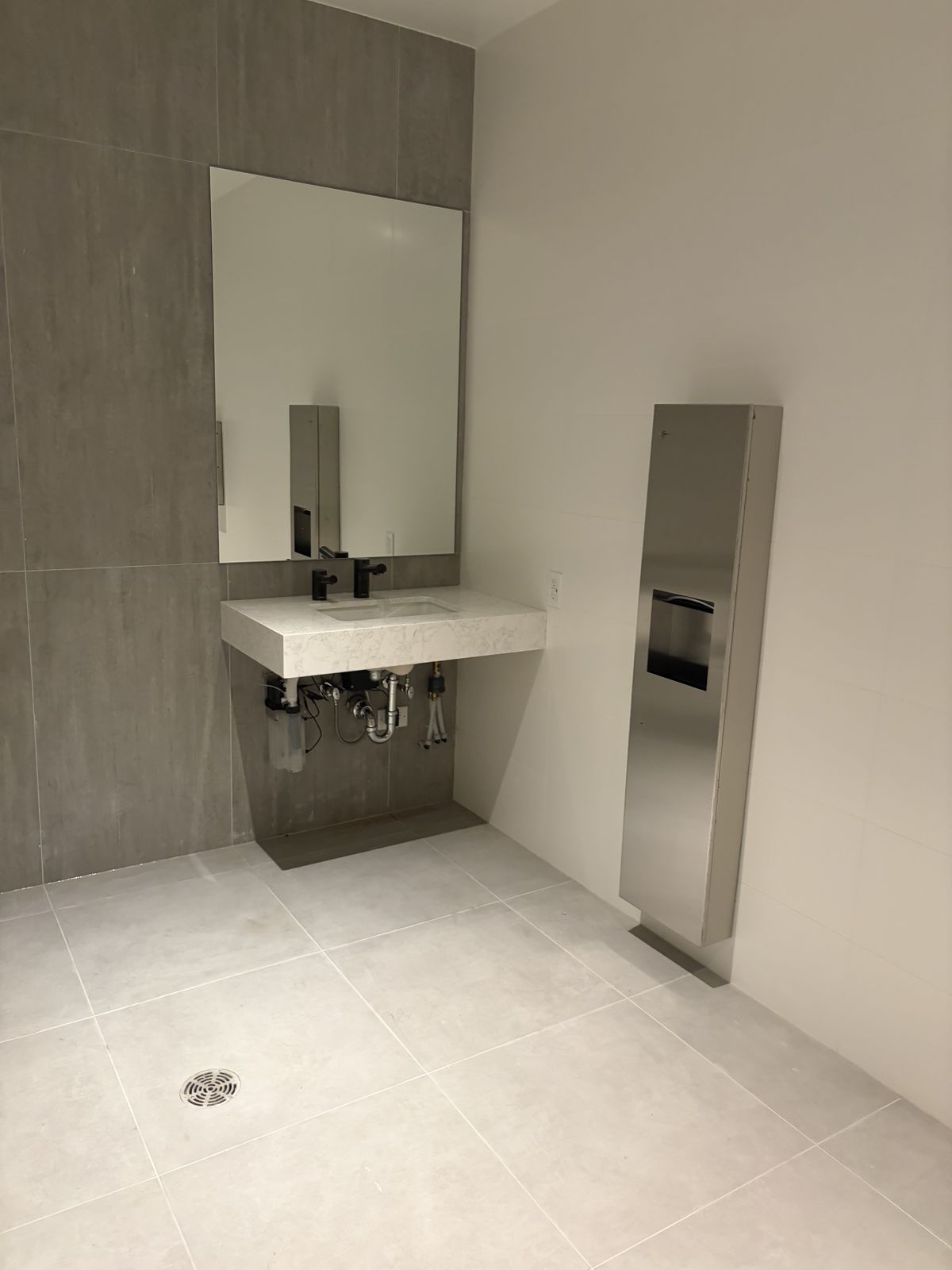 Accessible washroom with a wall-hung stone sink, large mirror and large-format grey tile