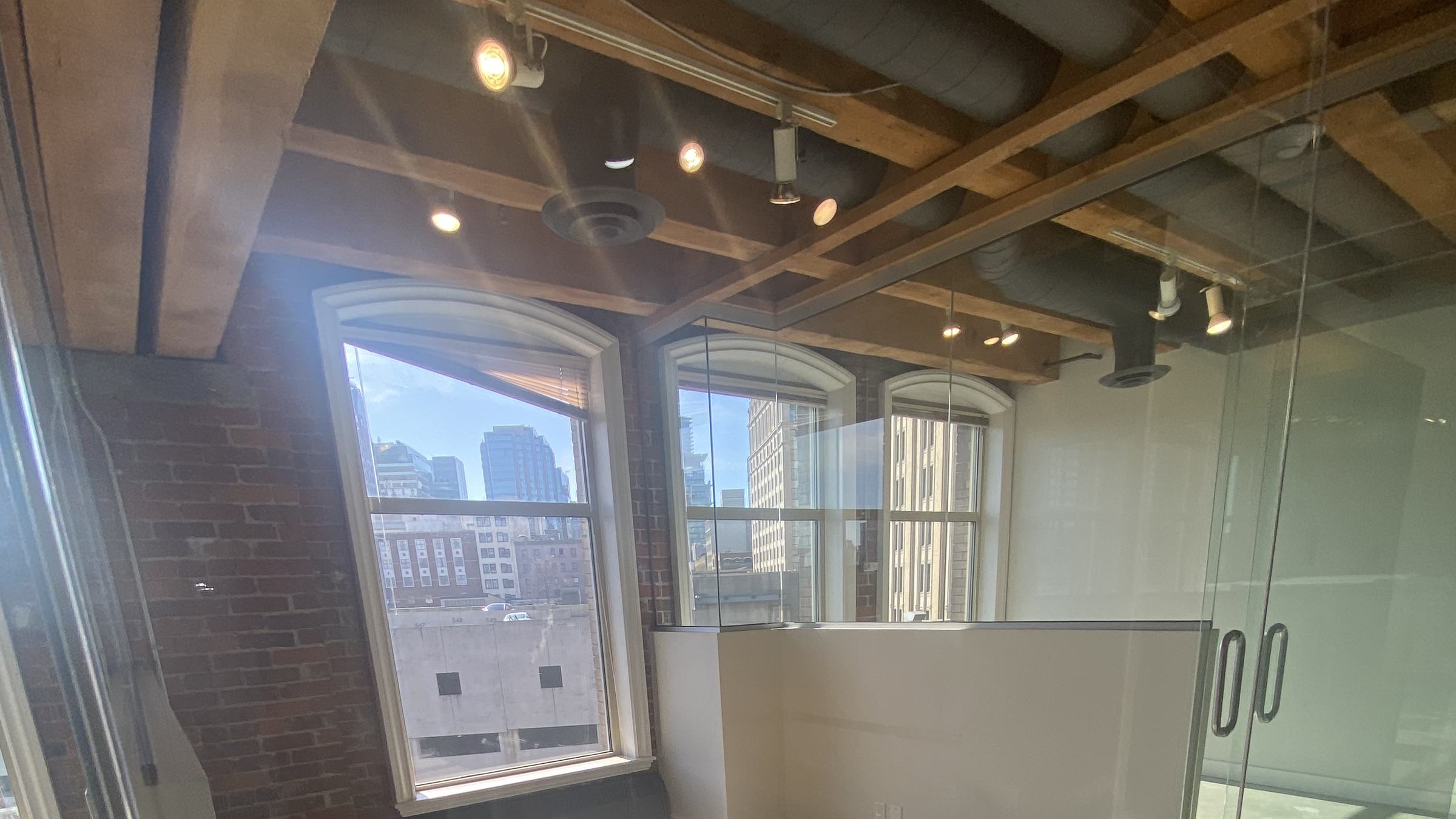 Heritage office interior with heavy-timber beams, exposed brick and arched windows overlooking downtown Vancouver